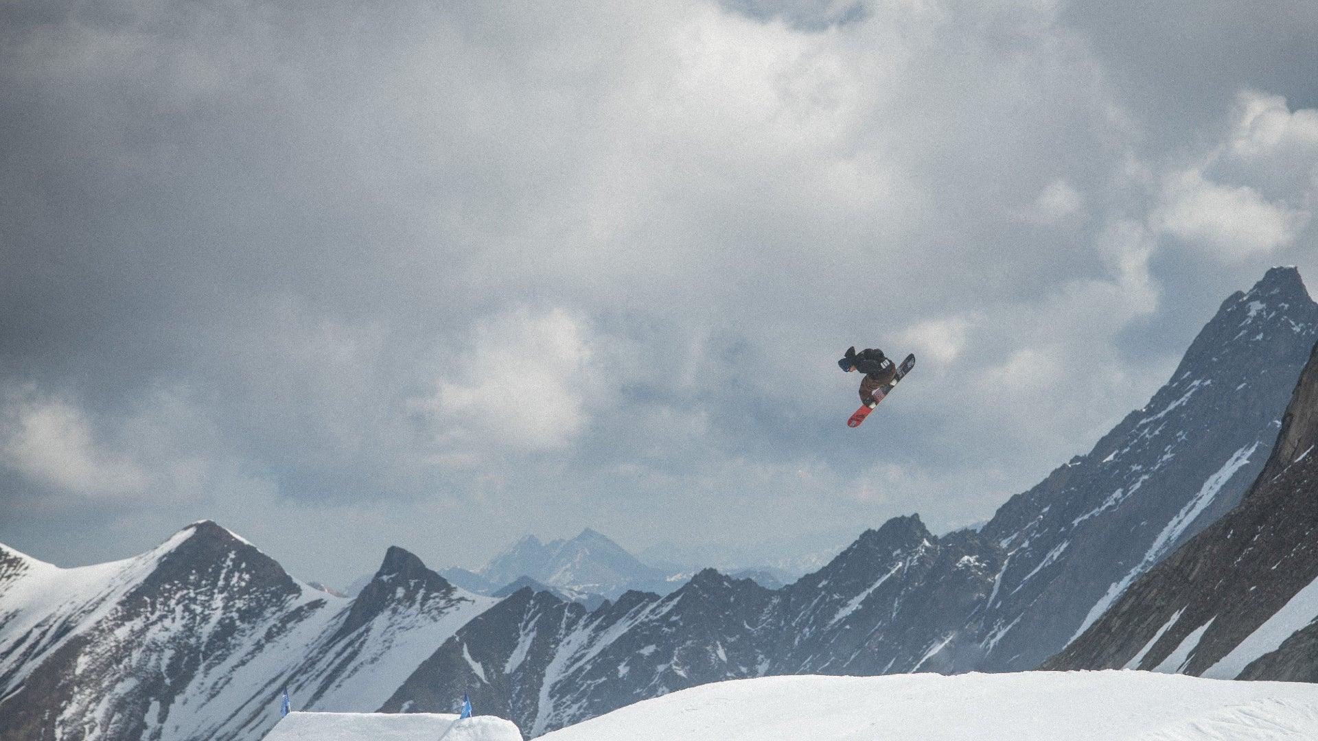 Person snowboarding in the air with a mountainous landscape in the background