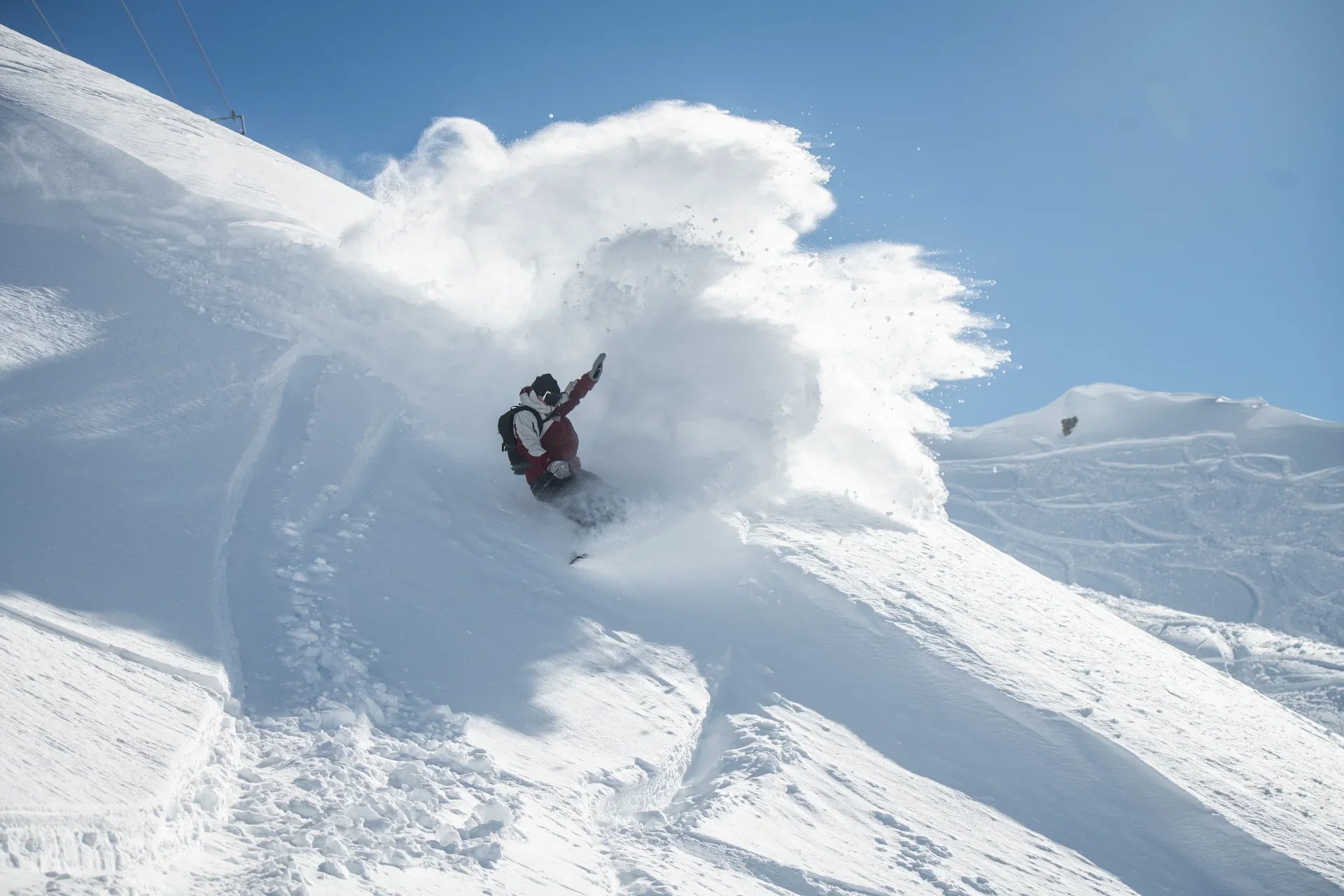 Person snowboarding down a snowy slope with a large cloud of snow behind them