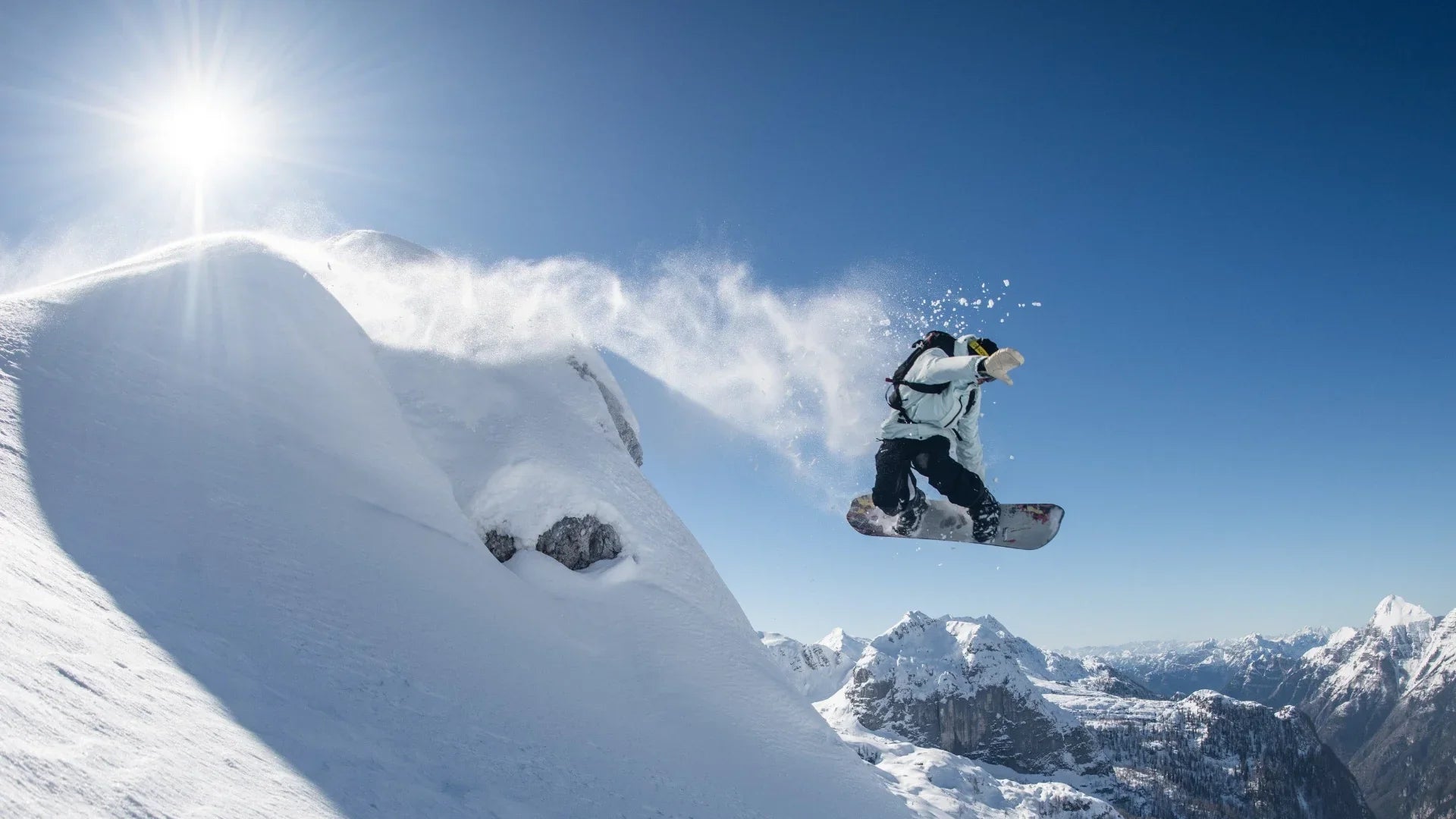 Person snowboarding off a ramp with snowy mountains in the background